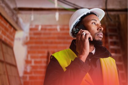 A construction worker in a hard hat and high-vis vest talks on his phone, managing operations and cash flow for labour hire.
