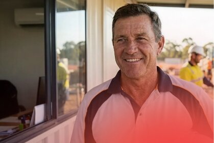 A smiling owner of a labour hire business in a polo shirt stands confidently at a labour hire site, reflecting successful business finance management.