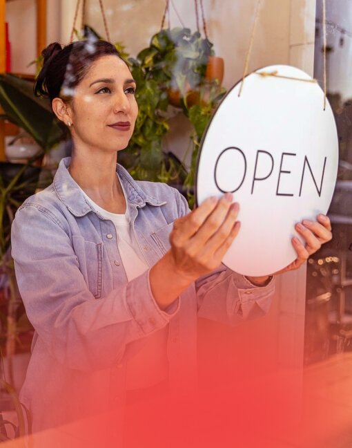 A female small business owner hangs an 'OPEN' sign, symbolising new opportunities for retail working capital.